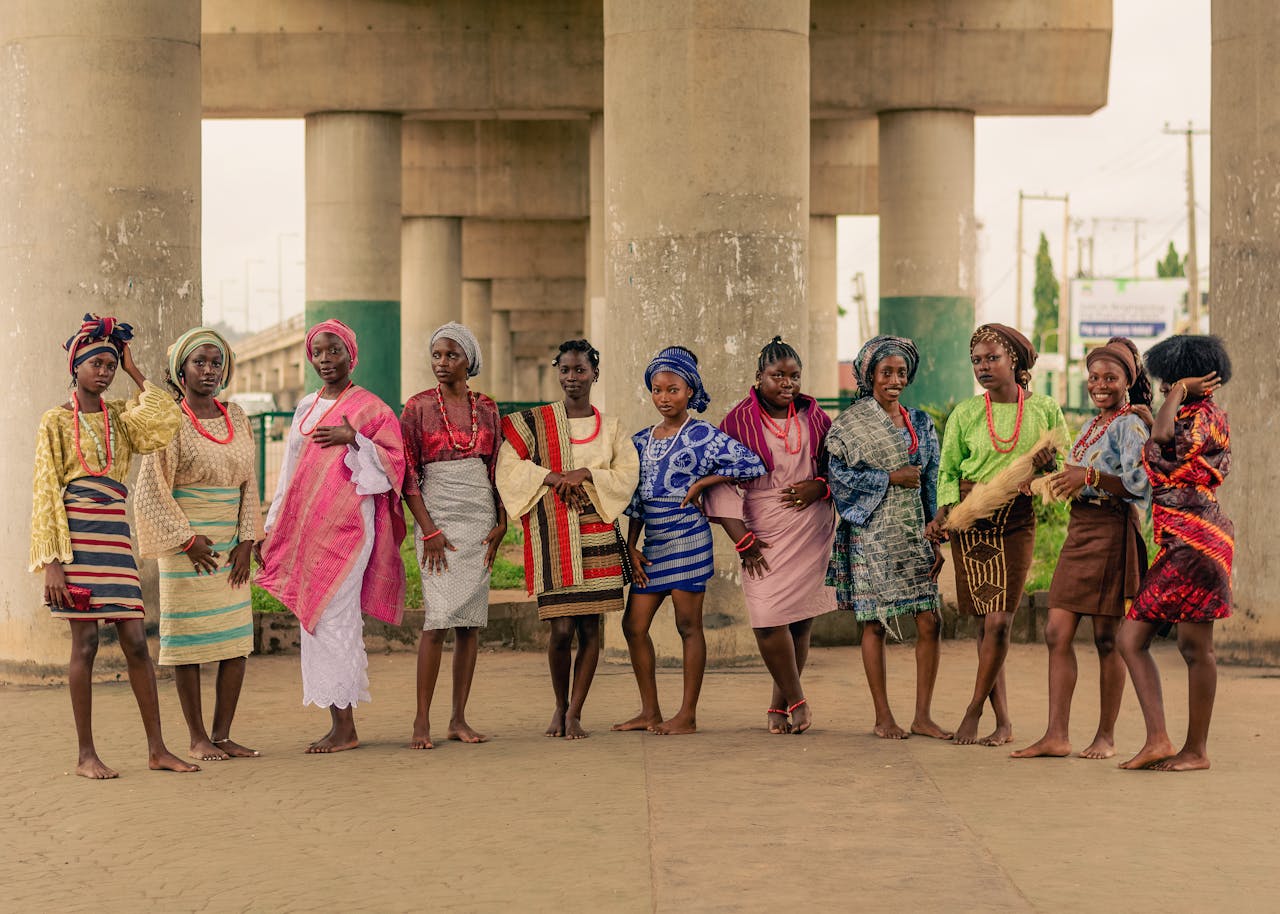 A group of women in vibrant traditional African attire pose under a bridge.